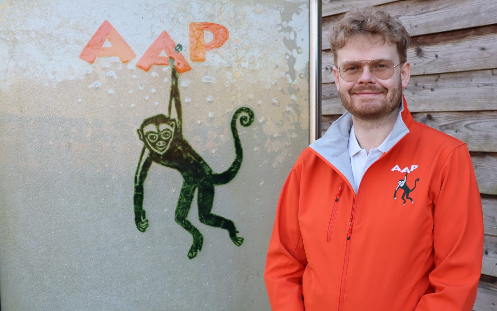 Auf dem Bild sieht man AAPs Pressesprecher Patrick Müller vor dem Schild mit dem Affenlogo von AAP.